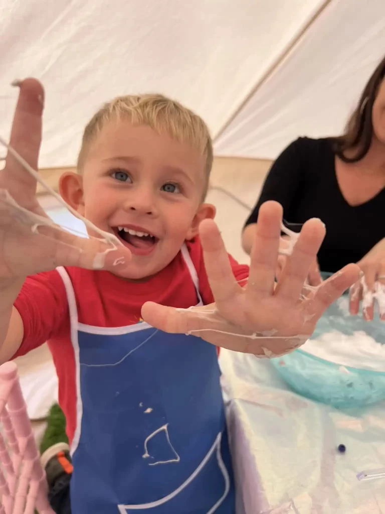 A young boy with his hands up at a table in a tent, holding the Ultimate Movie Night Setup Training Package - Transform Your Events.